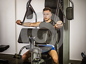 Muscular young man, training pecs on gym machine