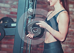 Muscular young smilling woman holds iron disk of barbell.