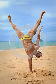 Muscular young undressed guy standing on hands on beach