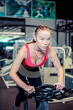 Muscular young woman working out on the exercise bike at the gym, intense cardio workout.