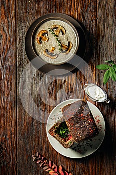 Mushroom cream soup decorated with sliced champignons and soup in bread on dark wooden table.