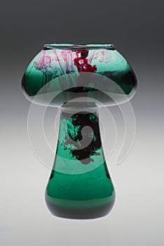 Mushroom shape glass jar with colorful food coloring dripping into water making unique patterns