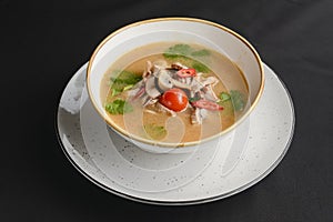 Mushroom soup of chicken broth, mushrooms, cherry tomato served in a white bowl over black background