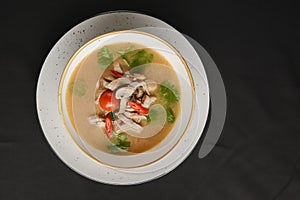 Mushroom soup of chicken broth, mushrooms, cherry tomato served in a white bowl over black background