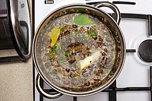 Mushroom soup with vegetables boiled in a metal pot on a gas stove, top view.