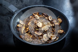 Mushrooms with sauce are cooked in a steaming black frying pan on the cooktop, preparing a vegetarian meal, copy space, selected