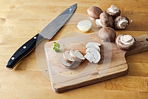 Mushrooms whole and sliced on a wooden cutting board and a kitchen knife, preparation for cooking a healthy vegetarian meal, copy