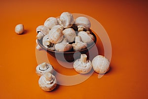 Mushrooms in a wooden bowl on an orange background. The small white champignon in a plate and scattered near it.