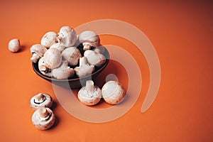 Mushrooms in a wooden bowl on an orange background. The small white champignon in a plate and scattered near it.