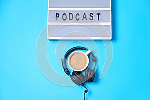 Music  background with Podcast word on lightbox,  headphones and cup of coffee on blue table, flat lay. Top view, flat lay, space