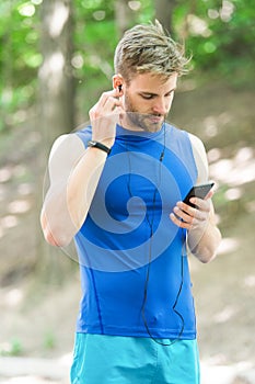 Music best companion to run. Man athlete on busy face set up play list, nature background. Sportsman training headphones