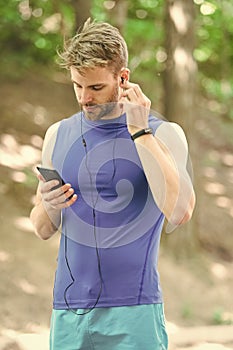 Music best companion to run. Man athlete on busy face set up play list, nature background. Sportsman training headphones