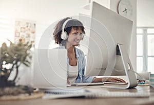 Music boosts creativity. an attractive young woman sitting alone at home and using her computer while wearing headphones