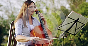 Music, cello and a woman reading sheet music outdoor in a garden with her orchestra or choir. Art, creative and