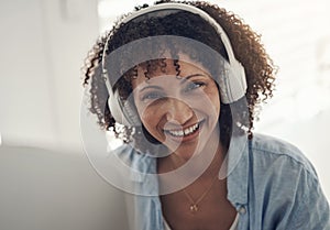 Music contains magic. an attractive young woman sitting alone at home and using her laptop while wearing headphones.