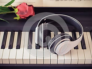 Music and entertainment concept.Music headphone on piano keyboard with red rose.vintage filtered