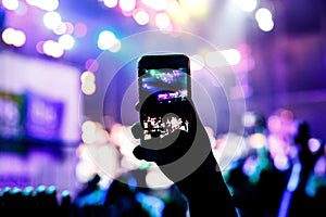 Music fans takes picture of stage in concert on smartphone.