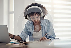 Music fuels my creativity. an attractive young woman sitting alone in her home and writing in a notebook while wearing