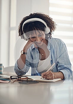 Music gets me in the zone. an attractive young woman sitting alone in her home and writing in a notebook while wearing