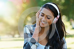 Music, headphones or happy woman in park to relax in garden, nature or field with smile or peace. Eyes closed, streaming