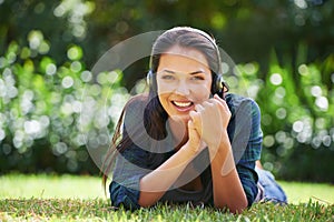 Music, headphones and relax for girl on grass outdoor in garden, lawn or forest for podcast, sound or streaming. Young