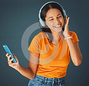 Music, headphones and woman streaming a song on phone or mobile app isolated against a studio background. Fun, sound and