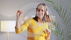 Music is her escape. Attractive young Caucasian woman listening music while dancing at home mowing hands enjoying favorite