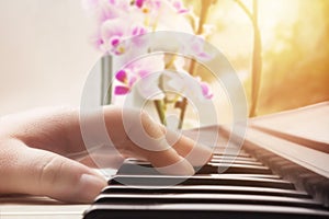 A music instrument and orchid. Warm color toned photo of a caucasian woman music performers hand playing the piano. Vintage piano