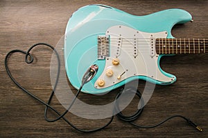 Music love concept. Wire jack heart guitar. Light blue electric guitar in a wood texture