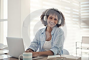 Music is the magic that motivates me. an attractive young woman sitting alone at home and using her laptop while wearing