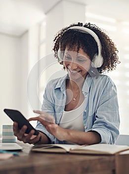 Music makes the days at home way better. an attractive young woman sitting alone at home and using her cellphone while