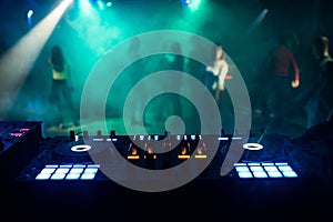 Music mixer in DJ booth at nightclub with people on dance floor and night atmosphere