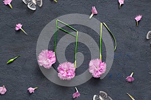Music notes with flowers and stems on a dark stone background. Musical summer abstraction top view