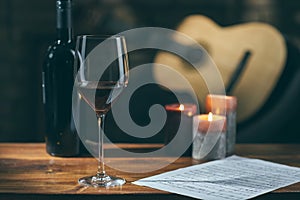 Music notes, wine and candle on table, with a guitar in the background