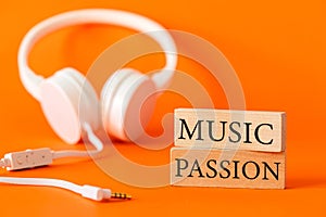 Music passion written on wooden blocks, White headphones for listening to music on a beautiful orange background, Concept related