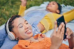 Music, phone and lesbian couple relax at picnic on grass, technology and streaming service app in nature. Cellphone