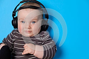 Music or podcast background with baby boy with headphones and microphone on blue table, flat lay. Top view, flat lay