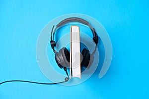 Music or podcast background Headphones with a book on blue table, flat lay. Top view, flat lay