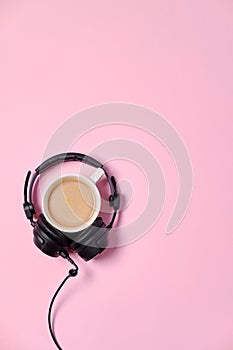 Music or podcast background with headphones and cup of coffee on pink table, flat lay. Top view, flat lay