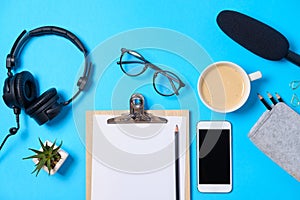 Music or podcast background with headphones, microphone, coffee and blank on blue table, flat lay. Top view, flat lay