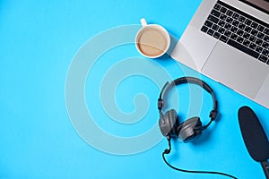 Music or podcast background with headphones, microphone, coffee and laptop on blue table, flat lay. Top view, flat lay