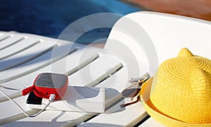 Music portable speaker is charged from the power bank via usb on a deck chair near the pool with beach accessories.