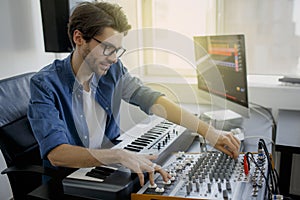 Music producer is composing a song on synthesizer keyboard and computer in recording studio. Man is working on sound