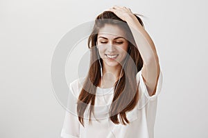 Music that recalls good memories. Portrait of attractive playful woman in white shirt touching hair and looking down