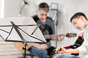 Music sheet standing in front of teacher and his young student playing guitar