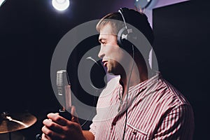 Music, show business, people and voice concept - male singer with headphones and microphone singing song at sound