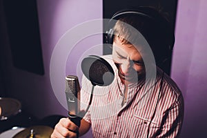 Music, show business, people and voice concept - male singer with headphones and microphone singing song at sound