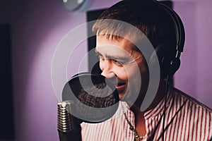 Music, show business, people and voice concept - male singer with headphones and microphone singing song at sound