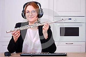 A music teacher provides online training in playing the flute. A female flautist teaches a flute lesson over the Internet, camera