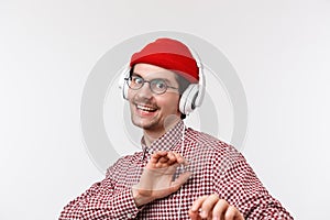 Music, technology and people concept. Carefree good-looking bearded male in glasses and red beanie dancing in headphones